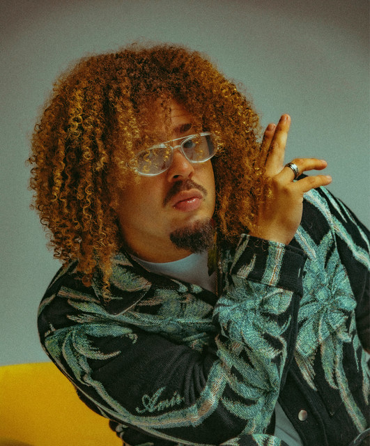 Portrait of the recording artist MAFFIO in clear-framed glasses and a patterned jacket.